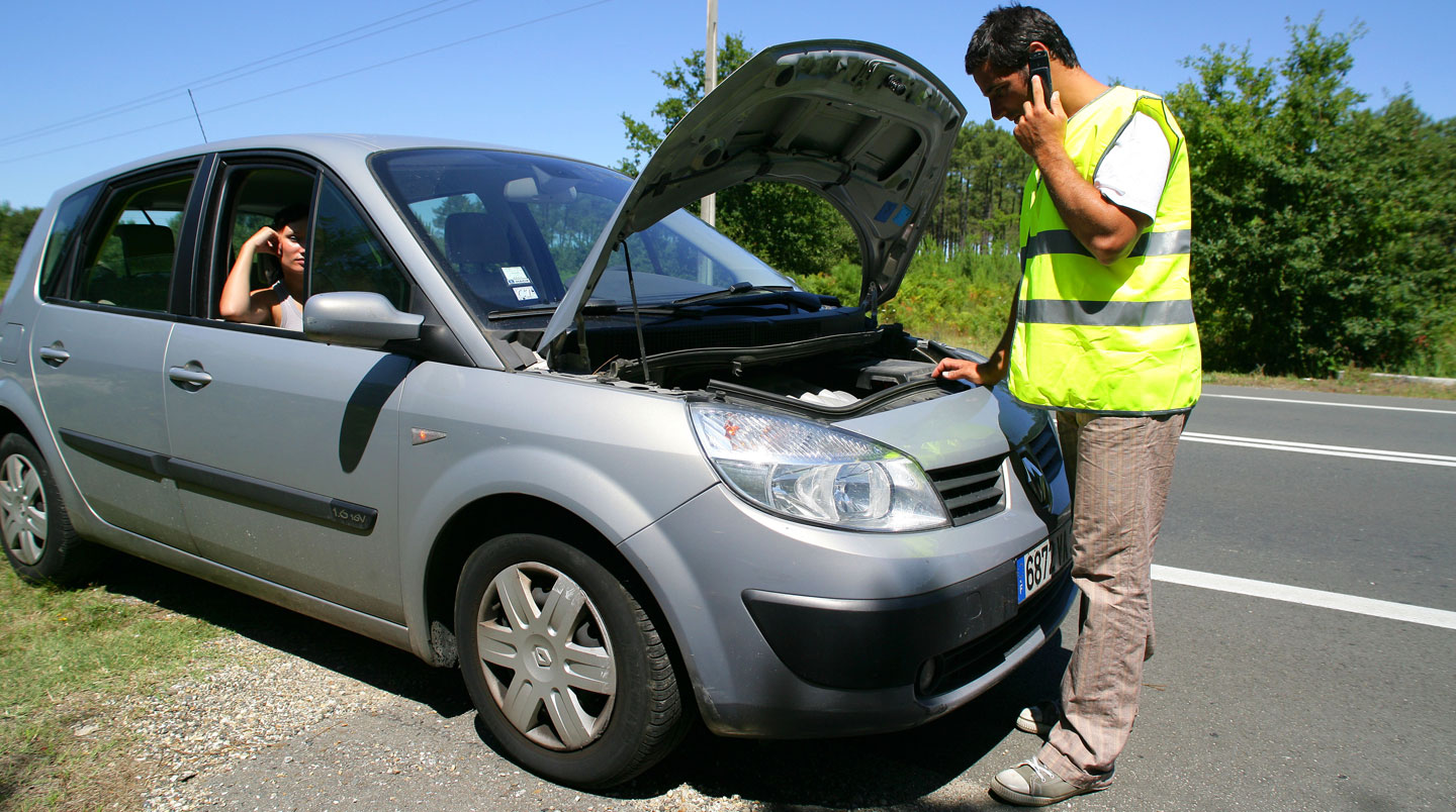 A mechanic inspecting a vehicle engine bay in a busy workshop setting with tools visible and other cars in the background